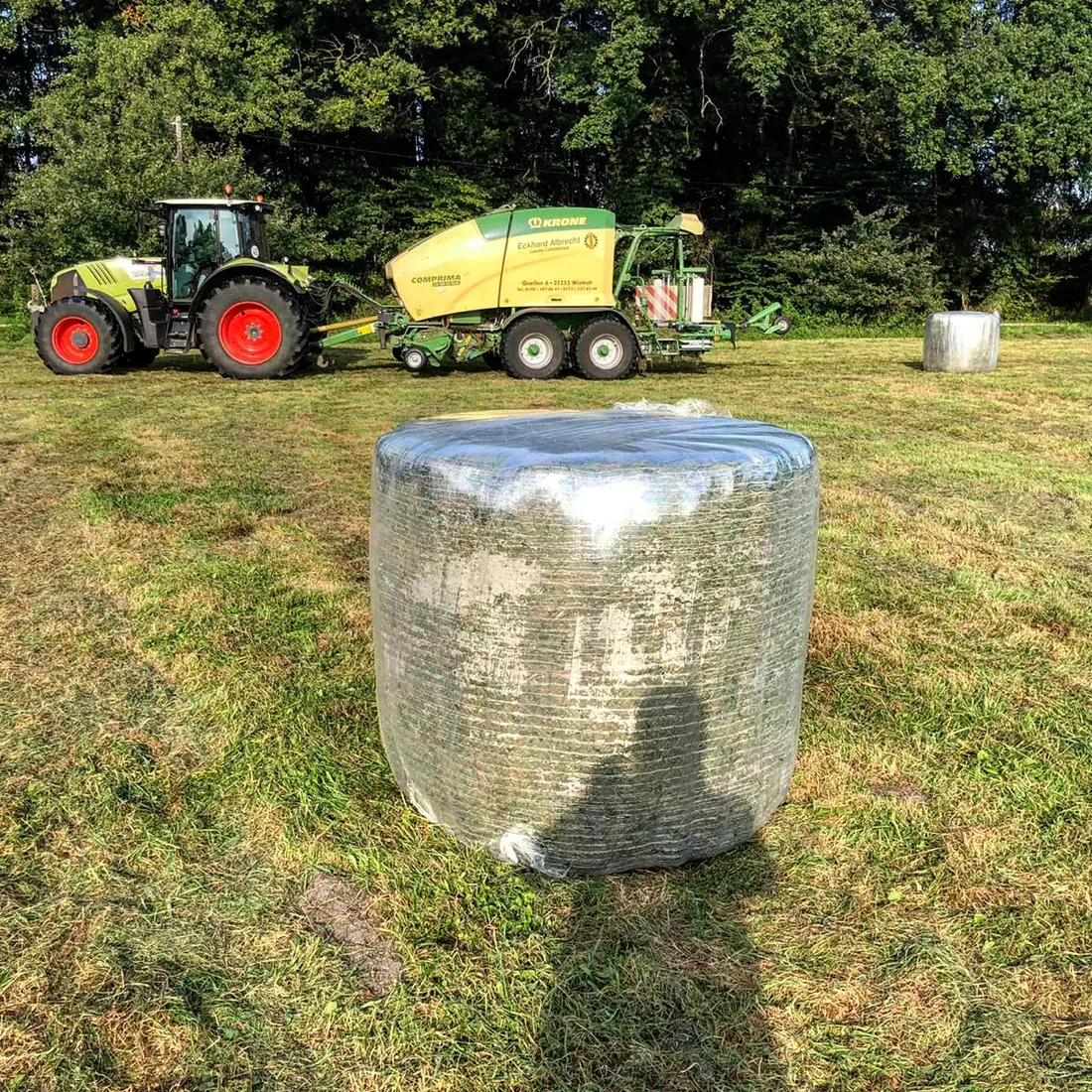 Mit transparenter Crystal-Folie gewickelter Rundballen auf dem Feld, Presse im Hintergrund